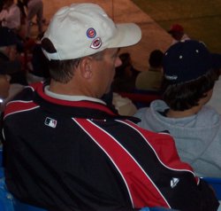 Wayne "Kriv-dog" Krivsky talking on a cell phone while wearing a hat with logos for the Arizona Diamonbacks, the Minnesota Twins, the Chicago Cubs, and the Cincinnati Reds